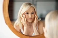 Brandi moteris žiūri į veidrodį ir vertina savo odos būklę